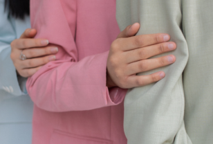 Women in pastel suits with hand on arm as a supportive gesture to relate with supporting menstrual health at work