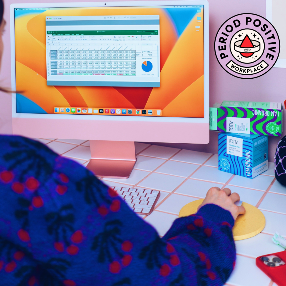 Girl on computer with period care on her desk to show it's a period positive workplace
